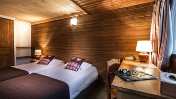 A wooden cabin room with two beds, a desk with a lamp, and a small window.
