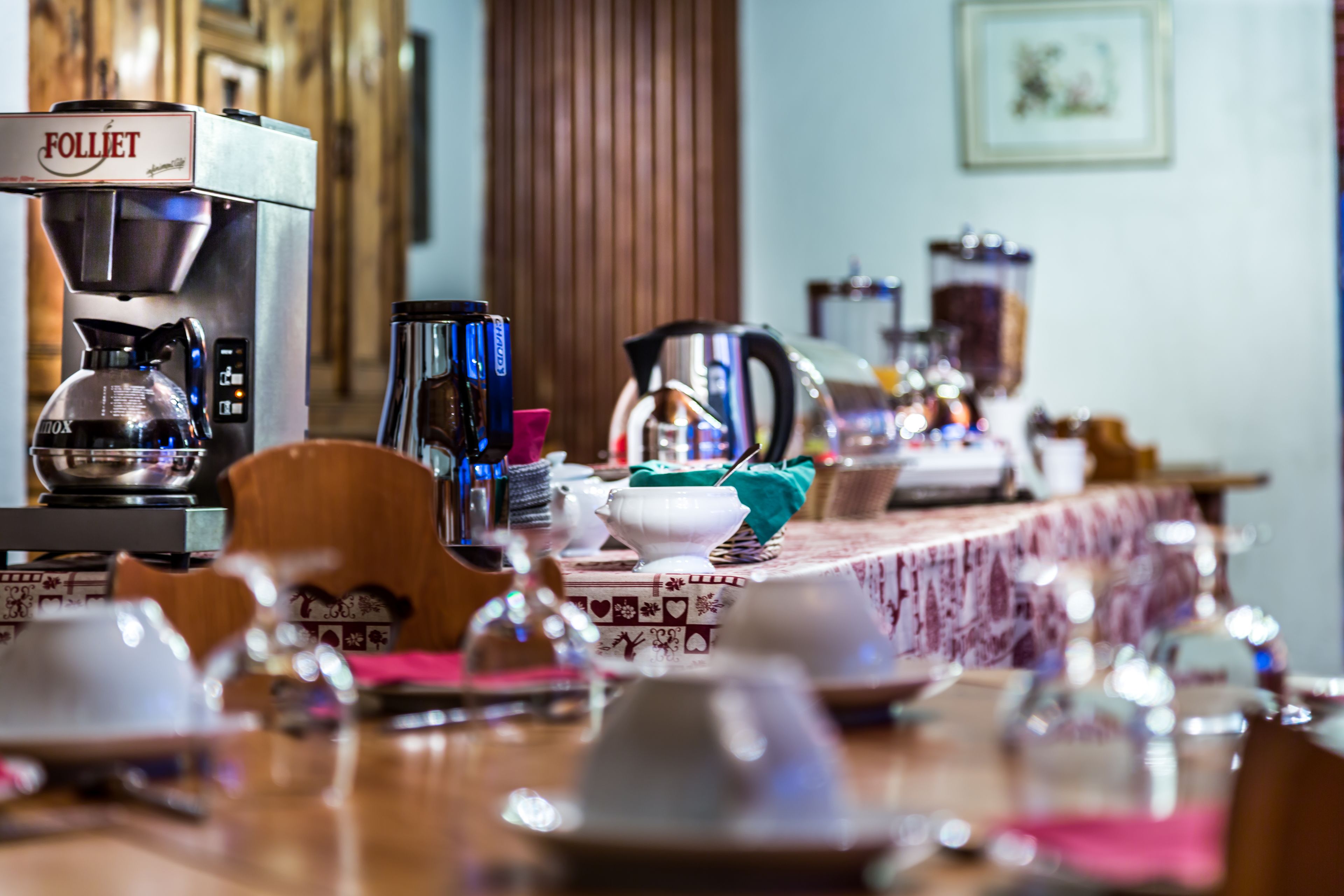 A dining area with a coffee machine, various cups, and a table set for a meal.