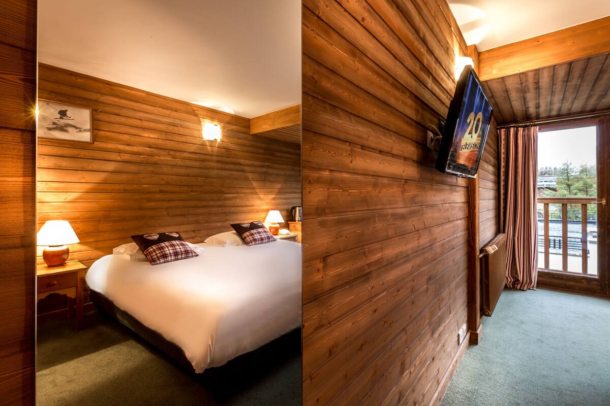 A wooden-paneled room with a bed, a nightstand with a lamp, and a television mounted on the wall.
