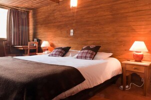 Una habitación de madera con una cama, dos mesitas de noche, una silla y una lámpara.
