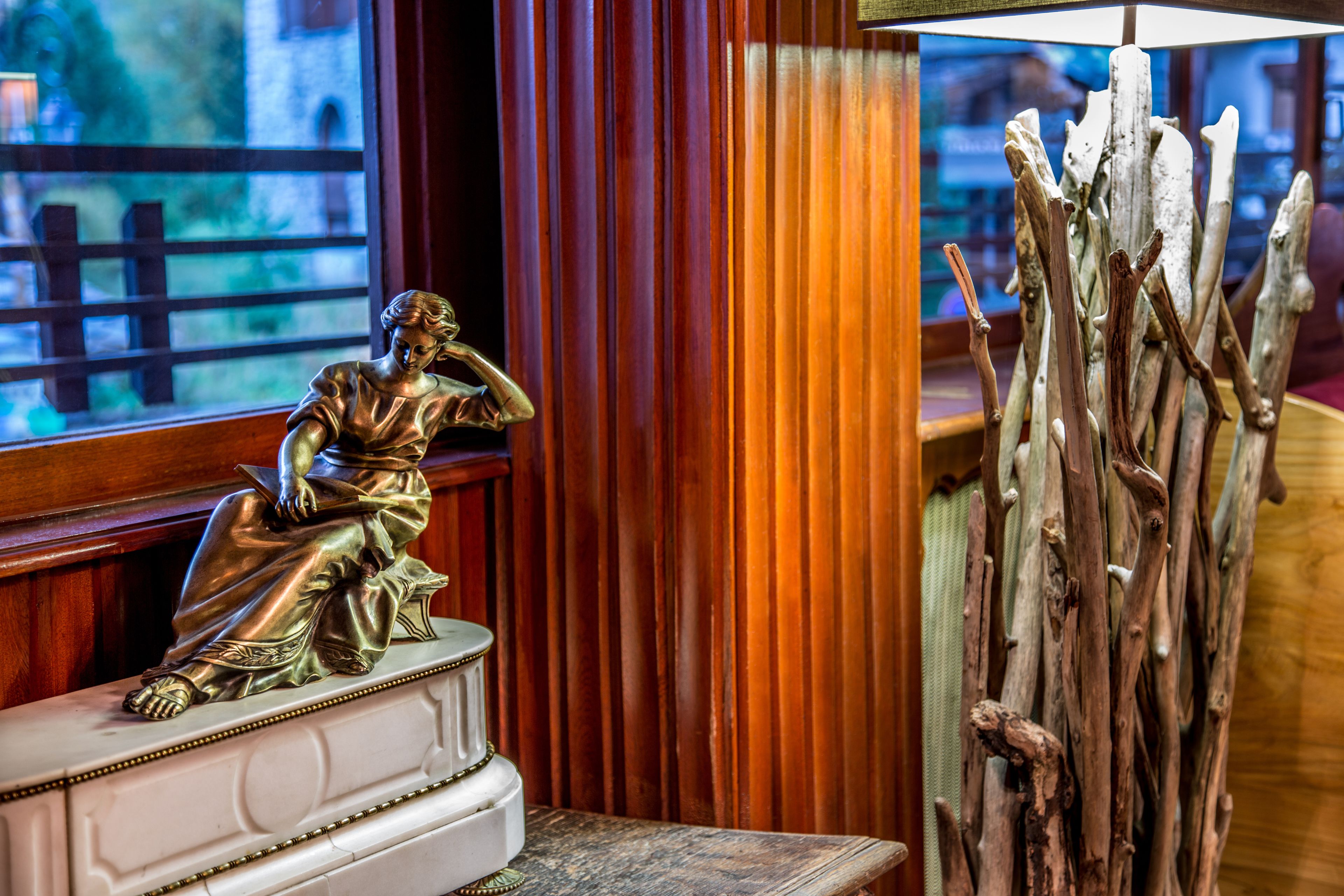 A statue on a pedestal, a window with a view of a wooden fence, and a collection of branches.