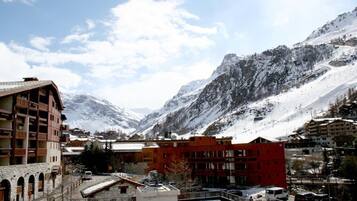 Un pueblo montañoso con picos nevados, un edificio rojo y una construcción de piedra con balcones.