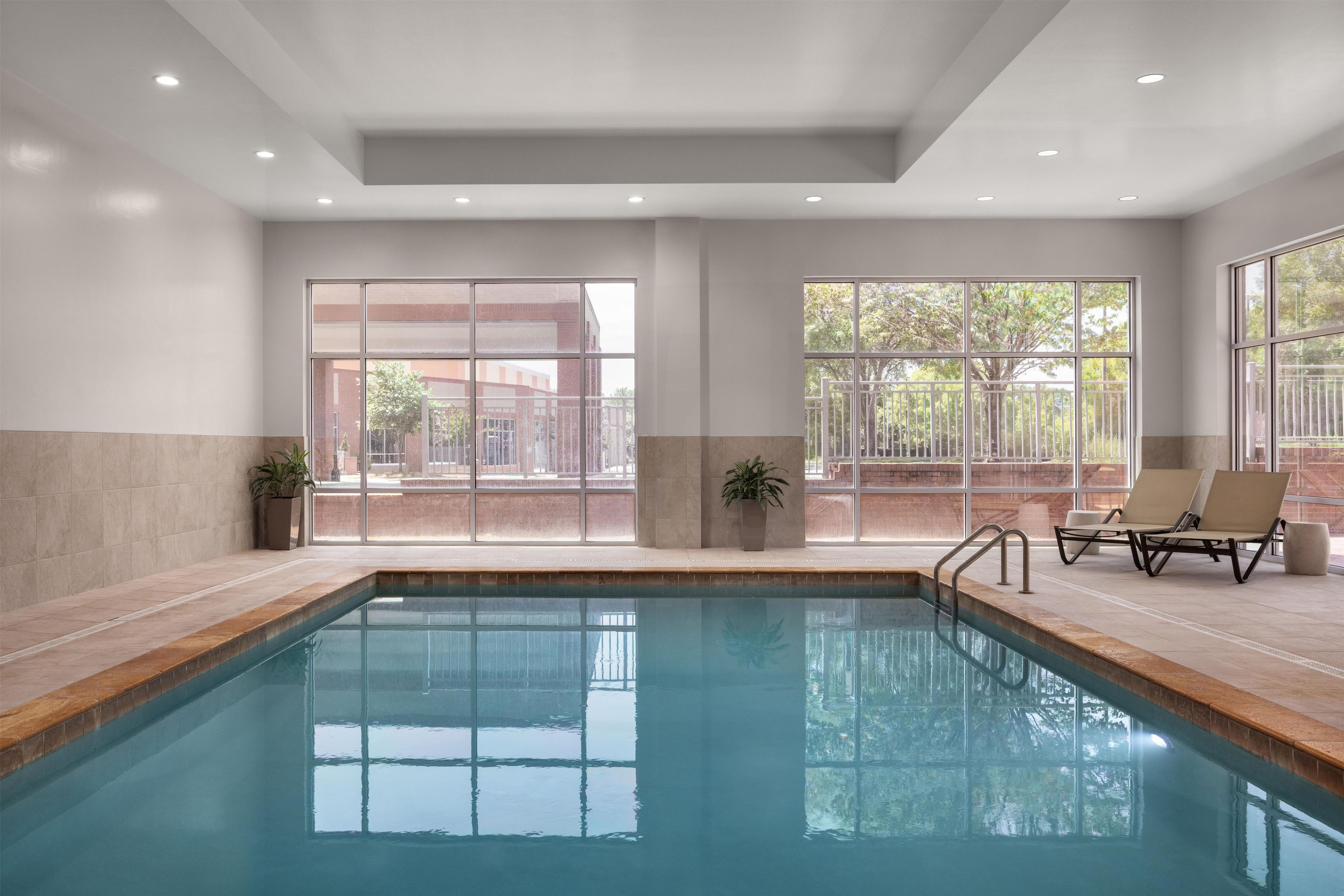 An indoor swimming pool with clear glass walls, a tiled floor, and a ceiling with recessed lighting.