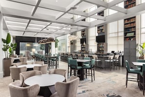 Un hall d’hôtel moderne doté d’un bar, de différents espaces de détente et d’une grande bibliothèque.