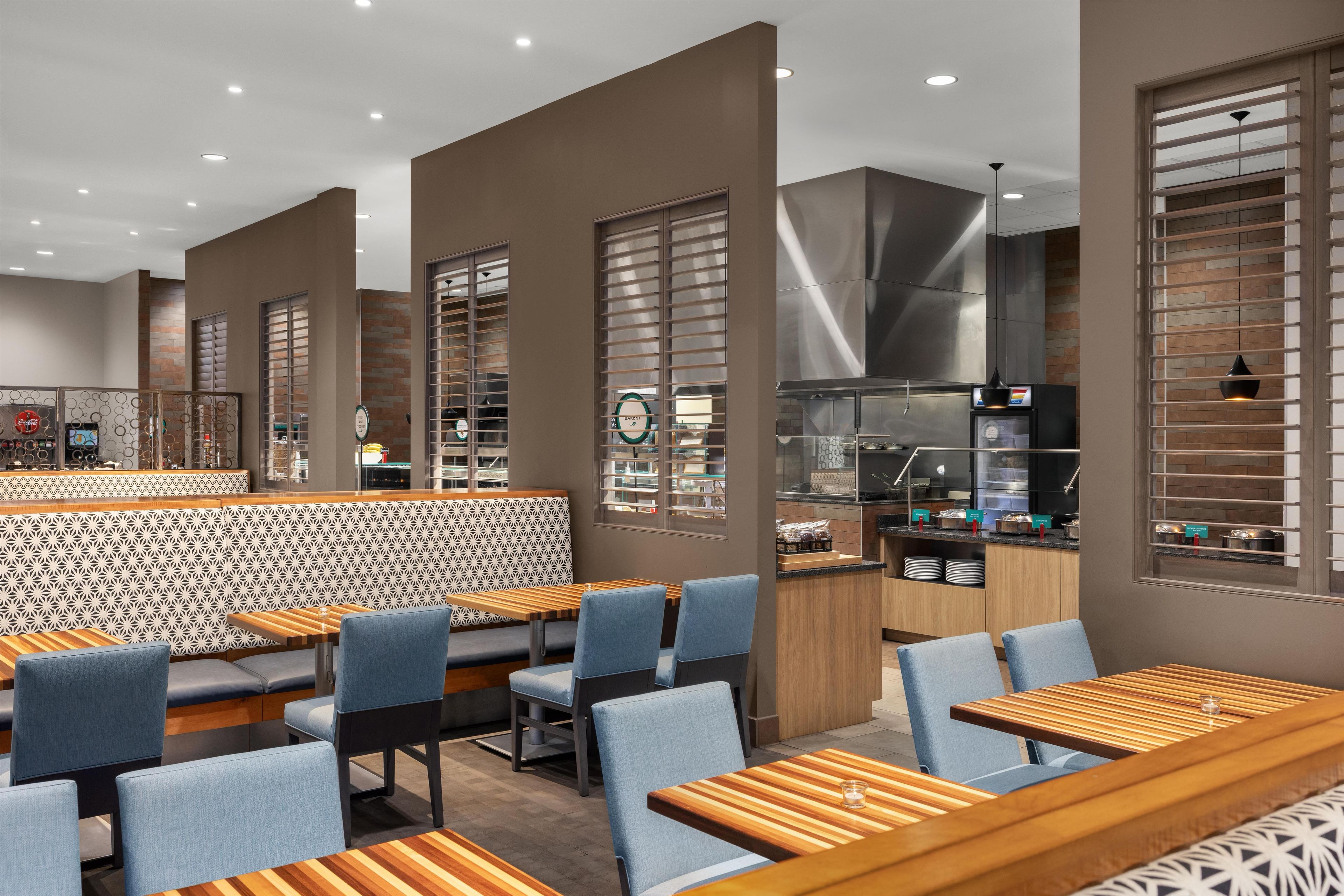 Un intérieur de restaurant moderne avec des banquettes et des tables, une cuisine ouverte et un mur décoré de motifs.