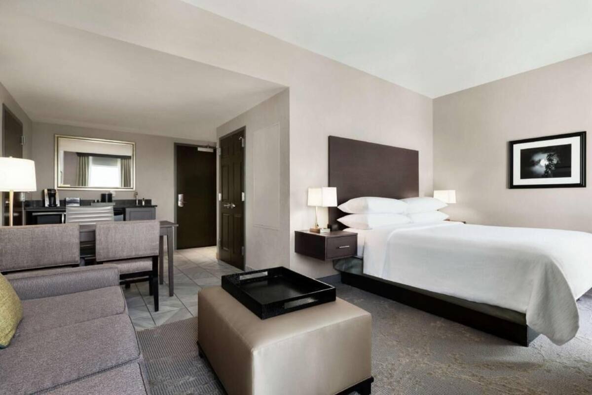 A hotel room with a bed, a sofa, a desk, a mirror, and a picture on the wall.