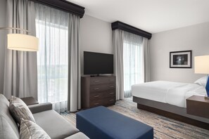 Une chambre d’hôtel avec un lit, un téléviseur posé sur une commode, un canapé et un bureau avec une lampe.