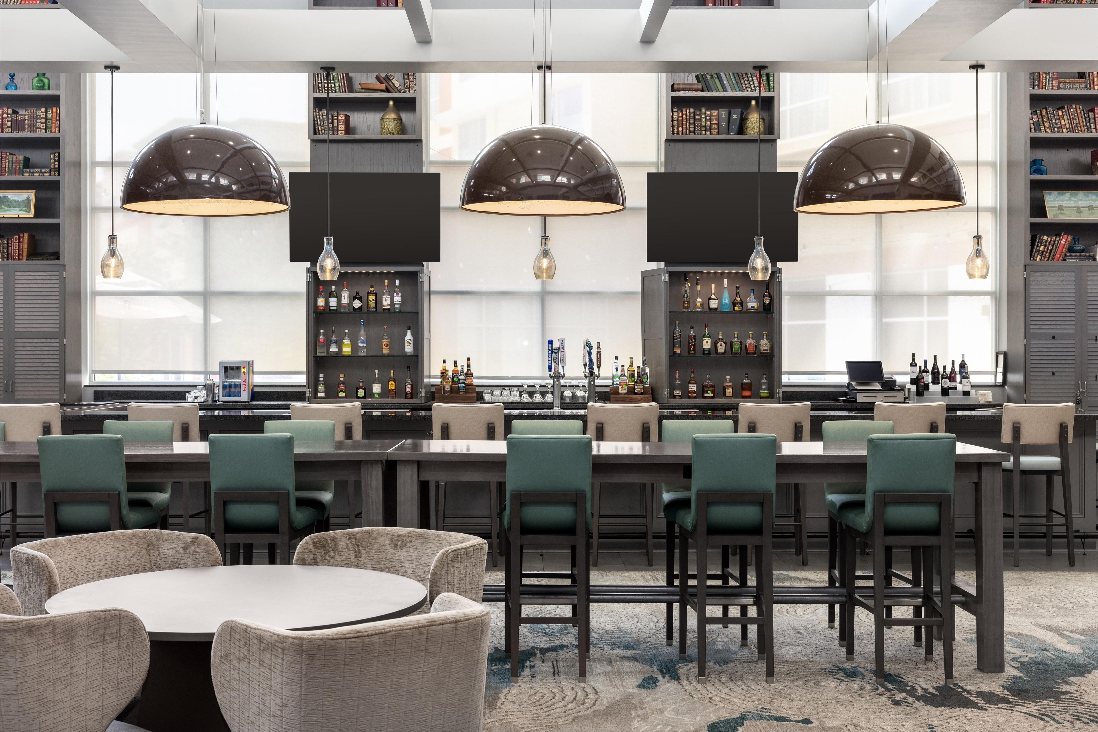 Een moderne bar met hoge plafonds, hanglampen en een bar voorzien van diverse flessen.