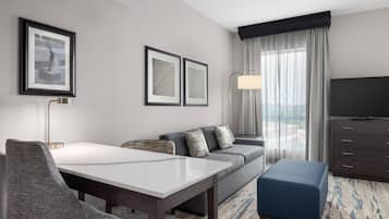 Een hotelkamer met een eettafel, een bank, een televisie en foto's in lijsten aan de muur.