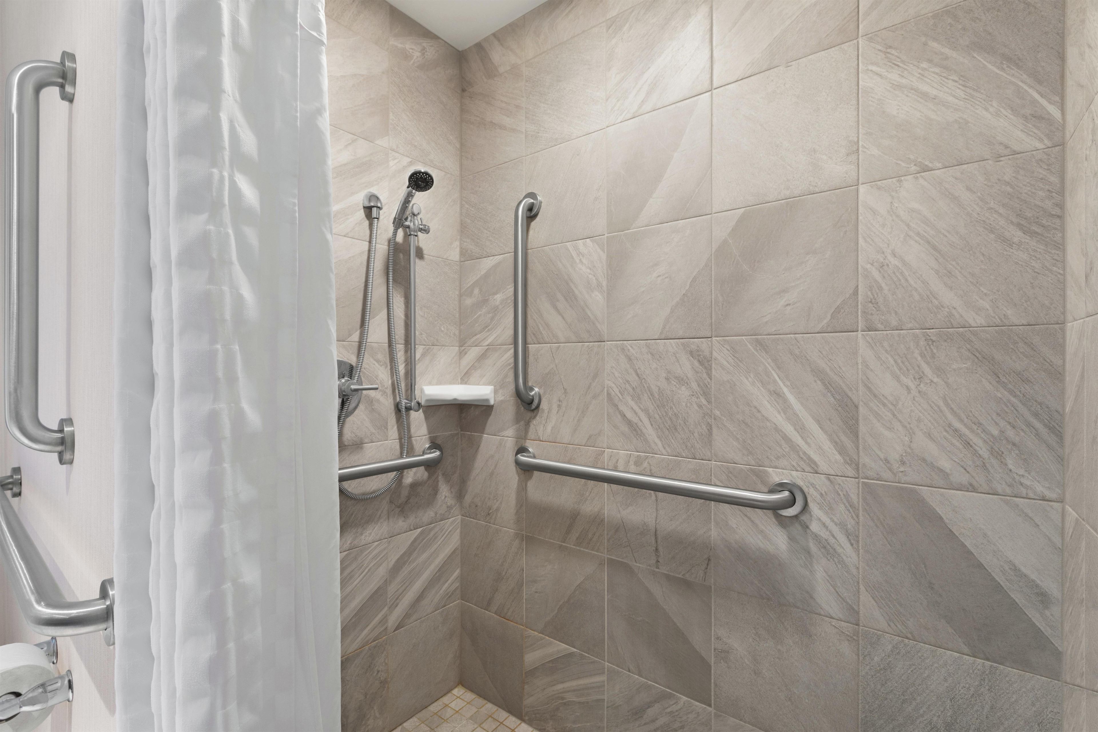 A shower area with grab bars, a showerhead, and a white curtain.