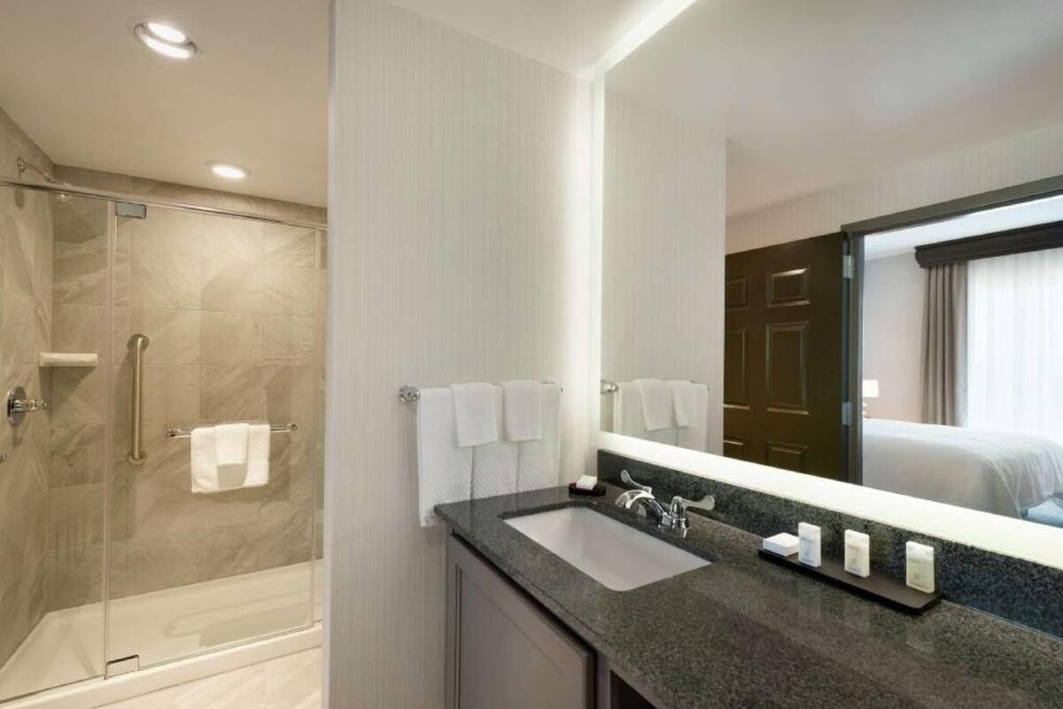 A hotel bathroom with a shower, sink, and mirror.