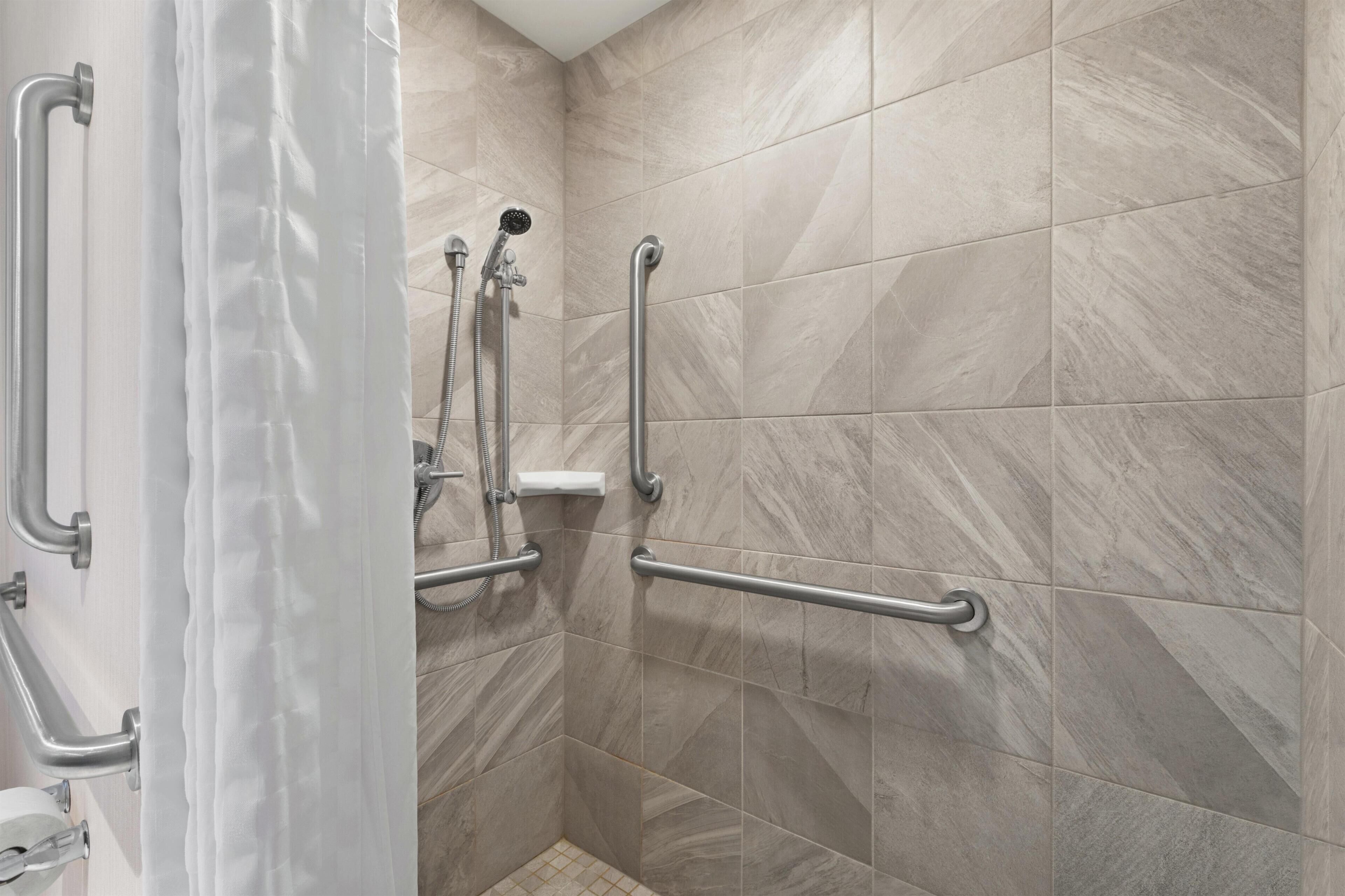 A shower area with grab bars, a showerhead, and a white curtain.