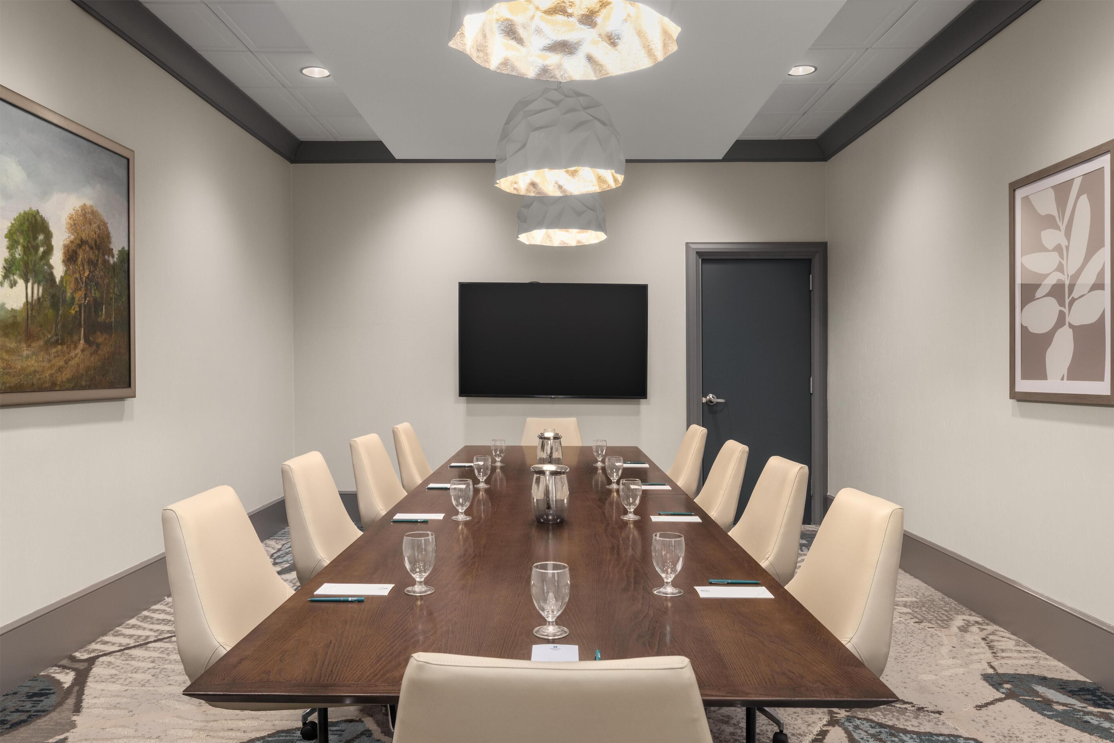 Une salle de conférence avec une longue table, des chaises, un téléviseur à écran plat et une porte.