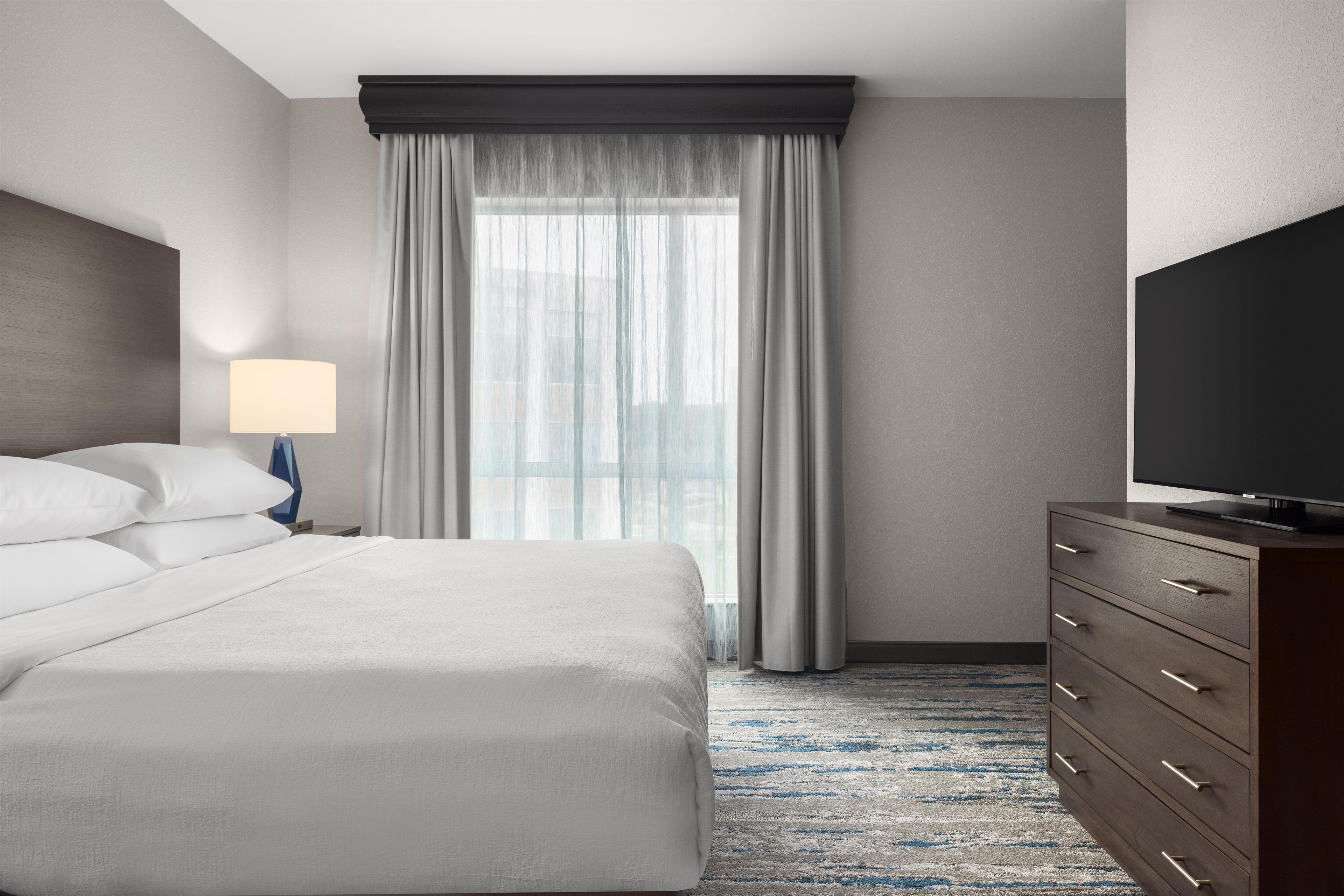 Een hotelkamer met een groot bed, een televisie op een dressoir en een raam met gordijnen.