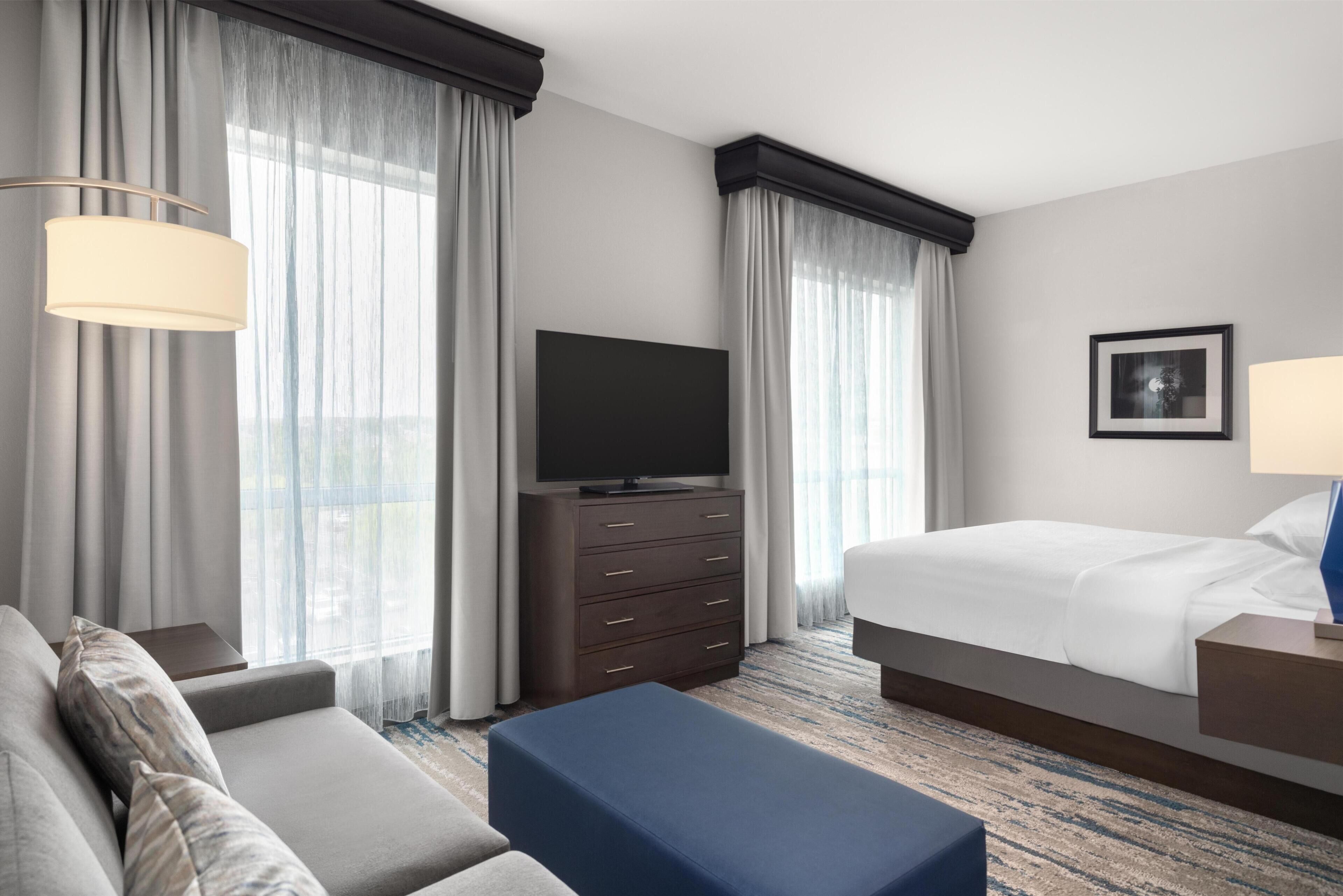 A hotel room with a bed, a TV, a dresser, a sofa, and a window with curtains.