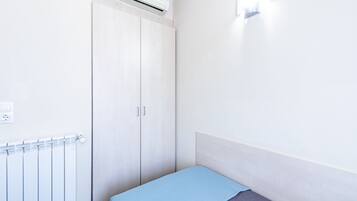 Ein kleines Zimmer mit einem Einzelbett, einer hellblauen Bettdecke, einem weißen Schrank und einem Heizkörper.