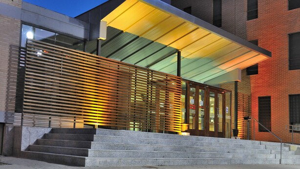 A modern building with a glass facade, a wooden slatted entrance, and a set of stairs leading to the entrance. - Residencia Universitaria Resa Giner de los Ríos - Hostel (Alcala de Henares)