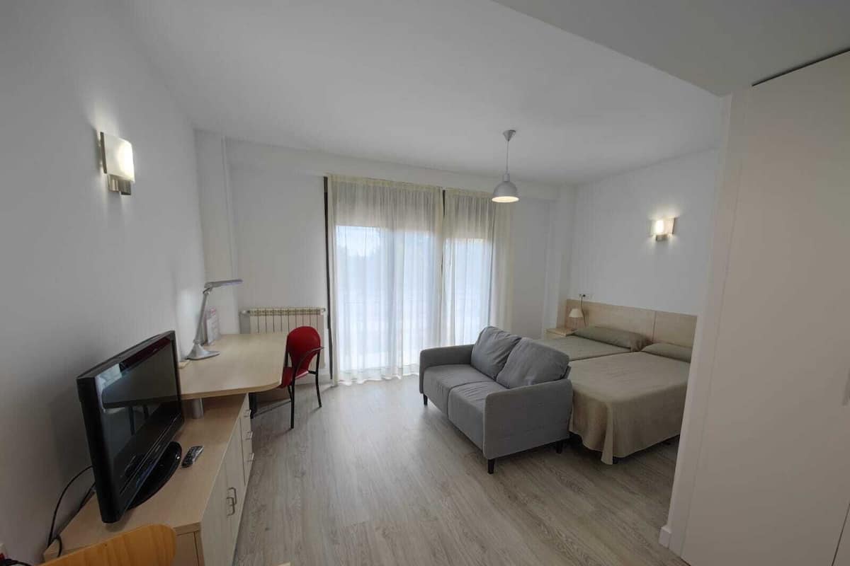 A compact hotel room with a bed, a sofa, a desk with a TV, and a chair.