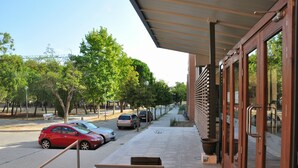 A covered outdoor area with a bench, a trash bin, and a pathway leading to a building with large windows and a door. - Residencia Universitaria Resa Giner de los Ríos - Hostel (Alcala de Henares)