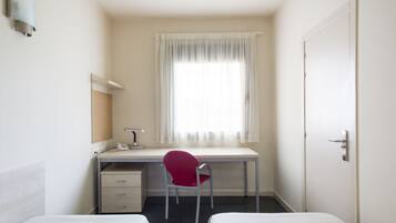 A small, clean room with a desk, a chair, and two beds.