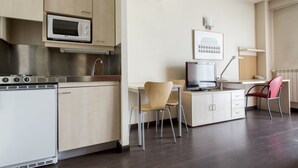 A modern kitchen with a microwave, stove, and sink. There is a dining area with a table and chairs. - Residencia Universitaria Resa Giner de los Ríos - Hostel (Alcala de Henares)