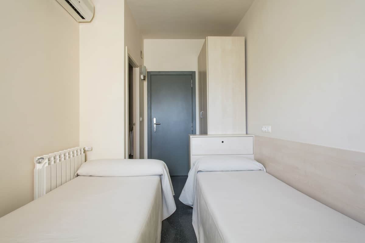 A hotel room with two single beds, a radiator, a door, and a light switch on the wall.