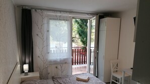 Un dormitorio con cama, mesita de noche, ventana con vista a un balcón y puerta que da al exterior.