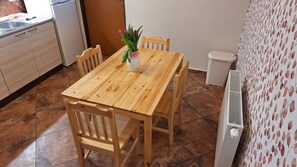 A wooden dining table with chairs, a vase with flowers, a white radiator, and a tiled floor.