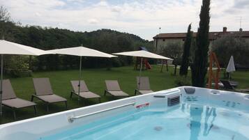 Relax by the pool with lounge chairs and a hot tub, surrounded by a lush lawn and a play area.