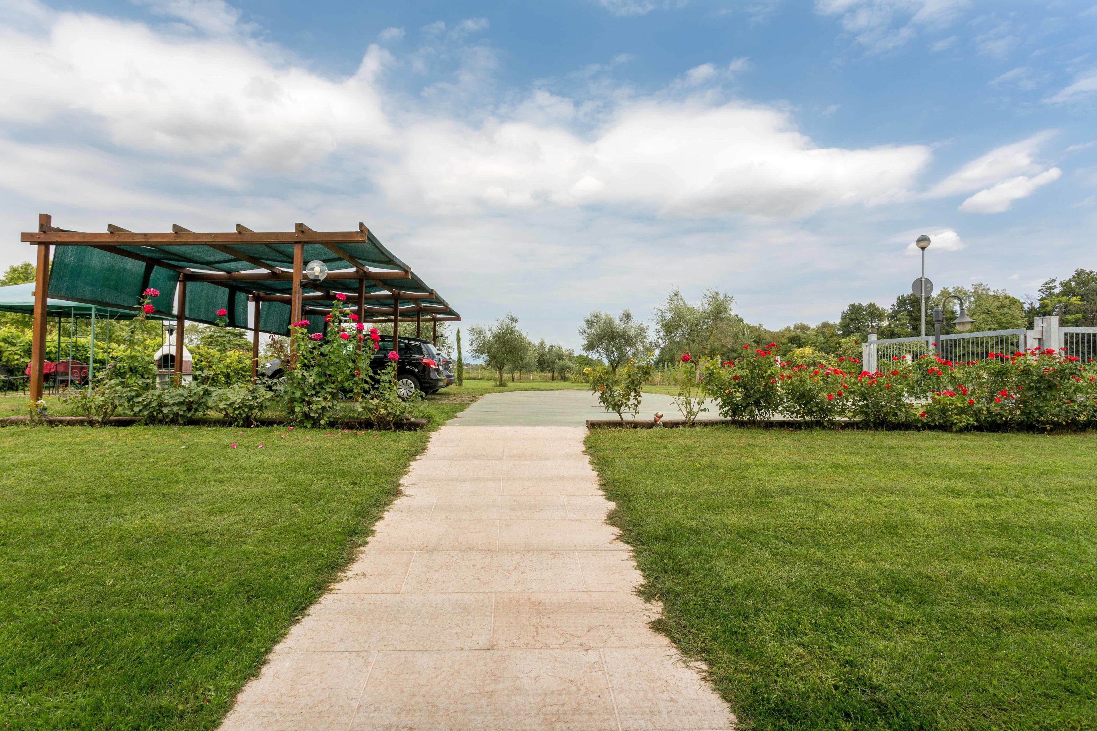 A pathway leading to a covered area with a pergola, surrounded by well-maintained grass and flowering plants.
