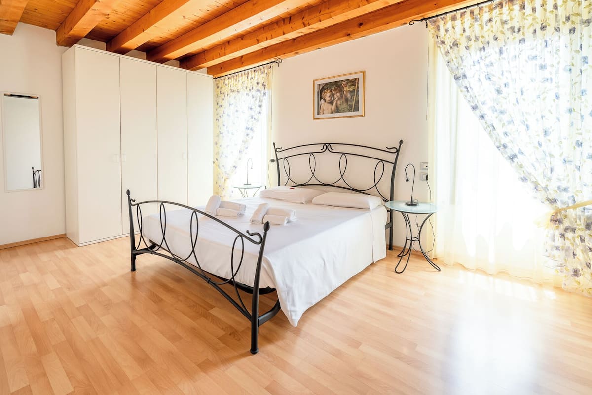 Een slaapkamer met een houten plafond, een metalen bedframe, een nachtkastje en een aan de muur hangend schilderij.