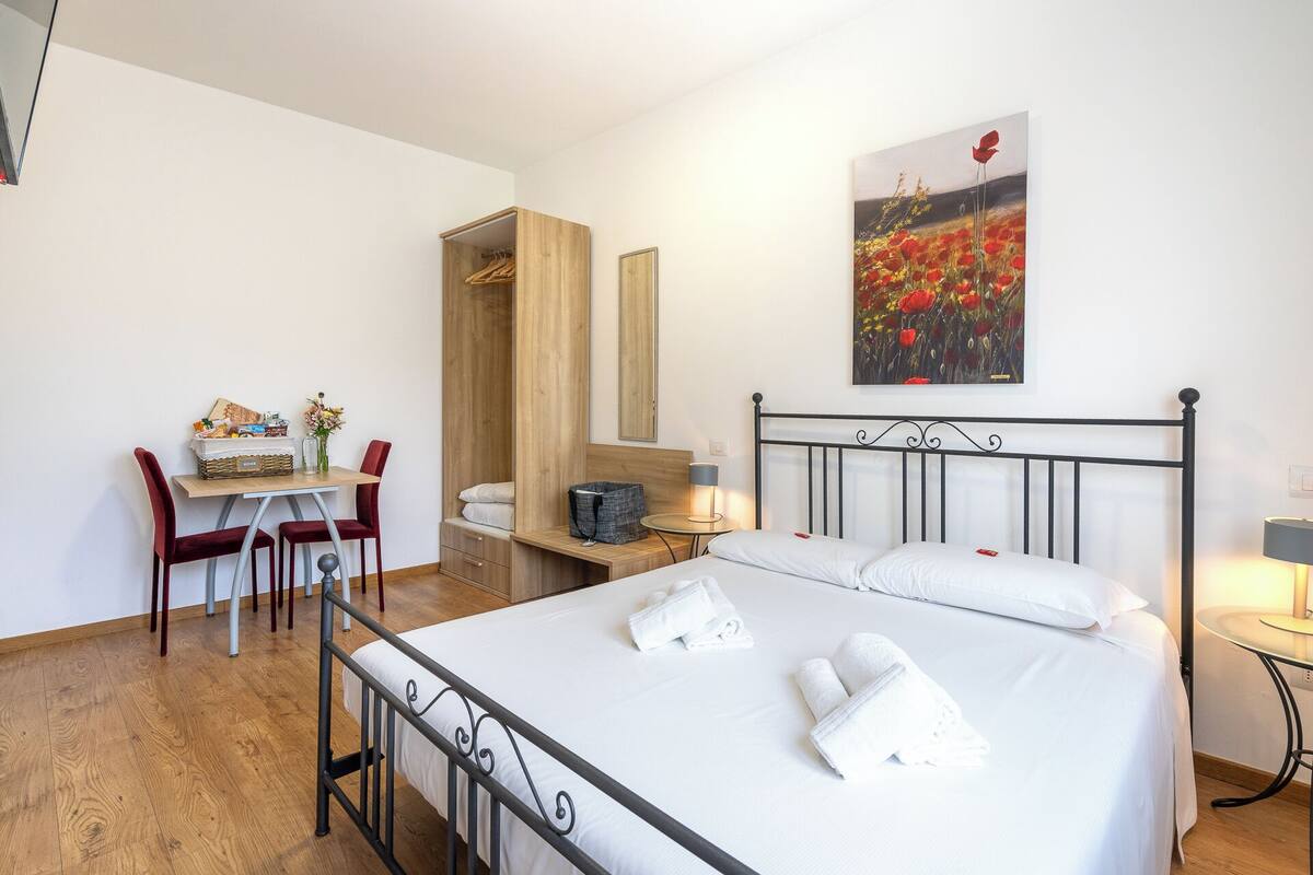 Een hotelkamer met een bed, een bureau met stoel, een kledingkast en een schilderij aan de muur.