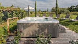 Un bain à remous sur une terrasse en bois, agrémentée de chaises longues et d’une pergola.