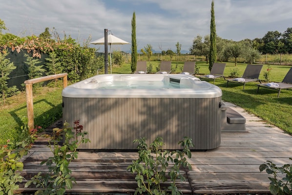Un bain à remous sur une terrasse en bois, agrémentée de chaises longues et d’une pergola.