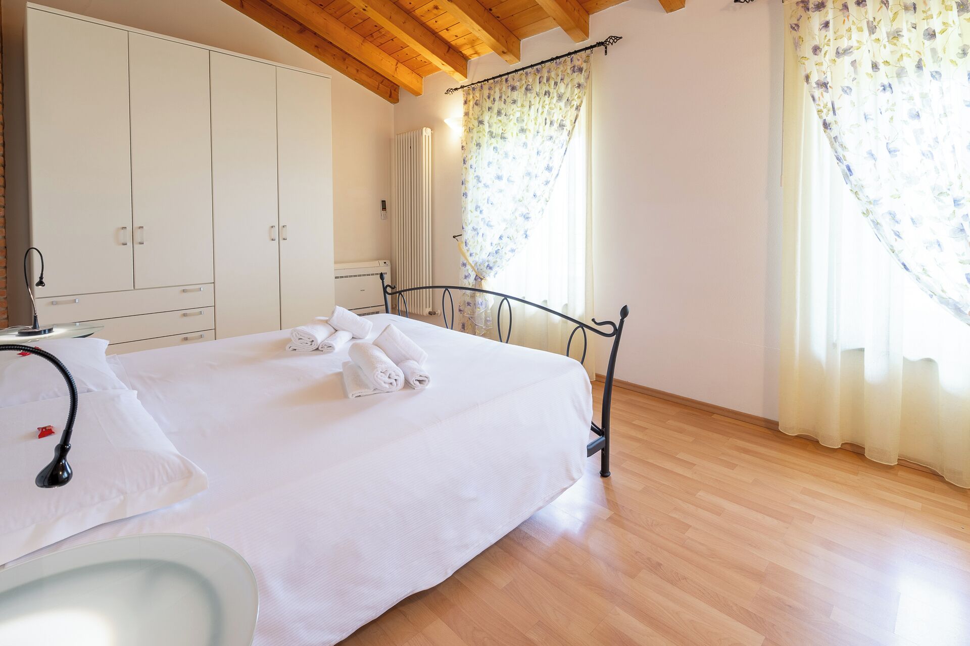A bedroom with a bed, a bedside table, a radiator, and curtains.