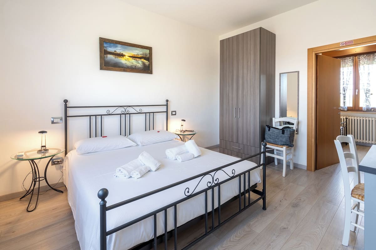 Een slaapkamer met een bed, nachtkastjes, een stoel, een kledingkast en een schilderij aan de muur.