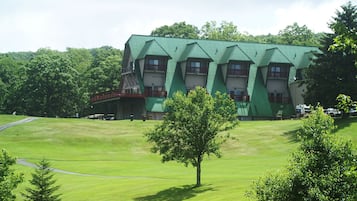 A building with a green roof and multiple windows, surrounded by a grassy area and trees.