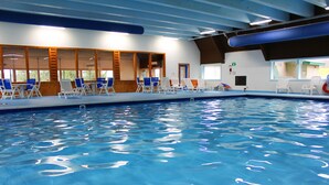 Una piscina interna con acqua cristallina e azzurra, circondata da lettini e porte in legno.