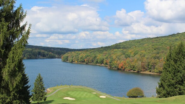 Un campo da golf con un lago, immerso tra alberi e colline.