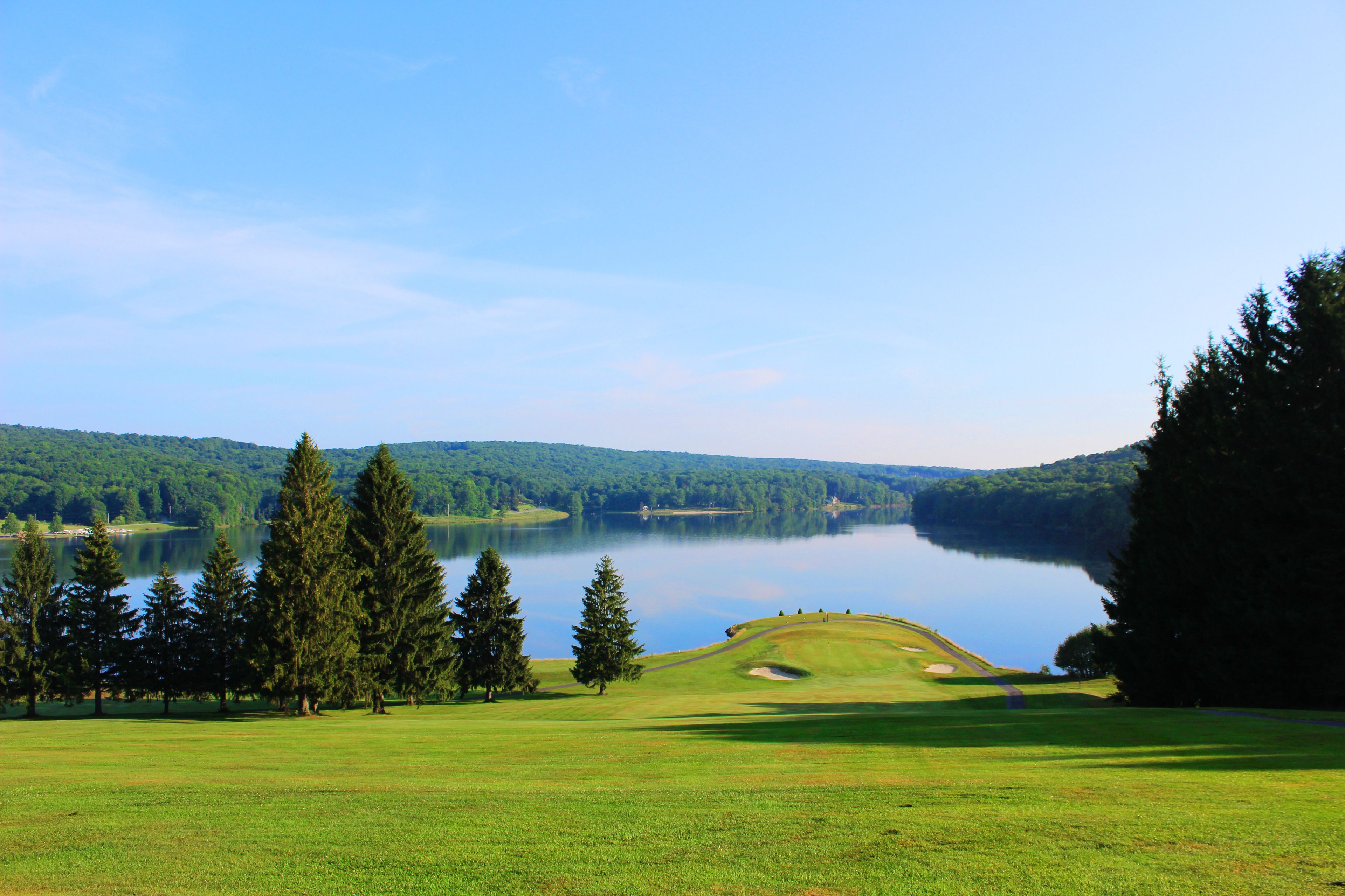 Un campo de golf con un lago, árboles y un cielo despejado.
