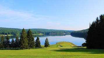 Un campo de golf con un lago, árboles y un cielo despejado.