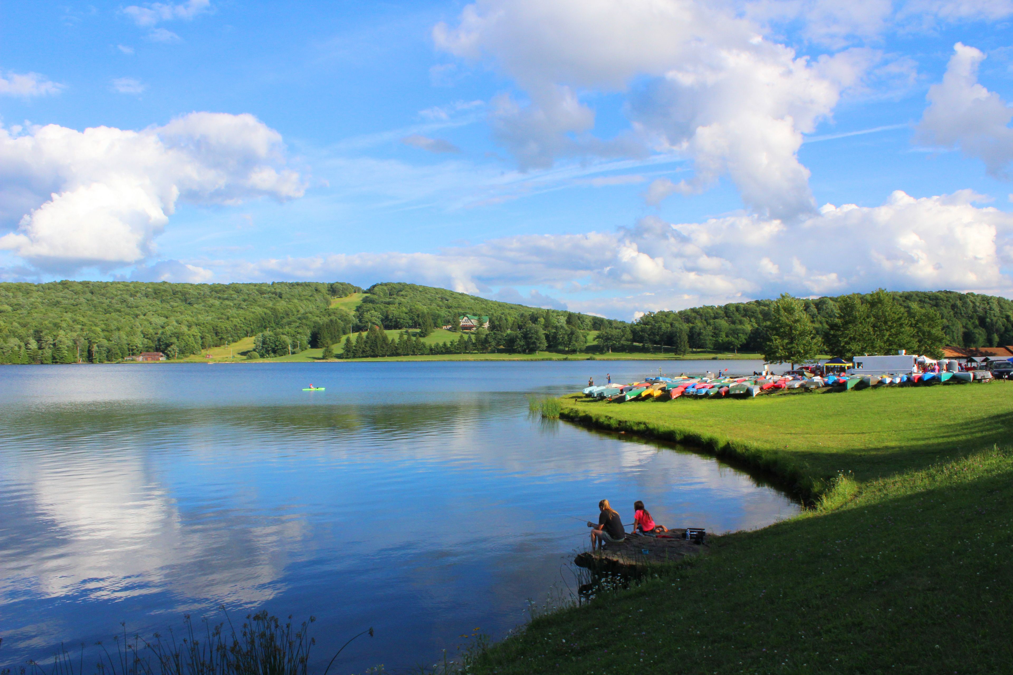 A lake with boats, a grassy area, and a few buildings in the background.