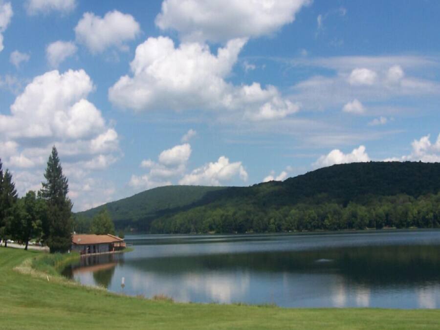 A lakeside view with a building on the shore, surrounded by greenery and hills.