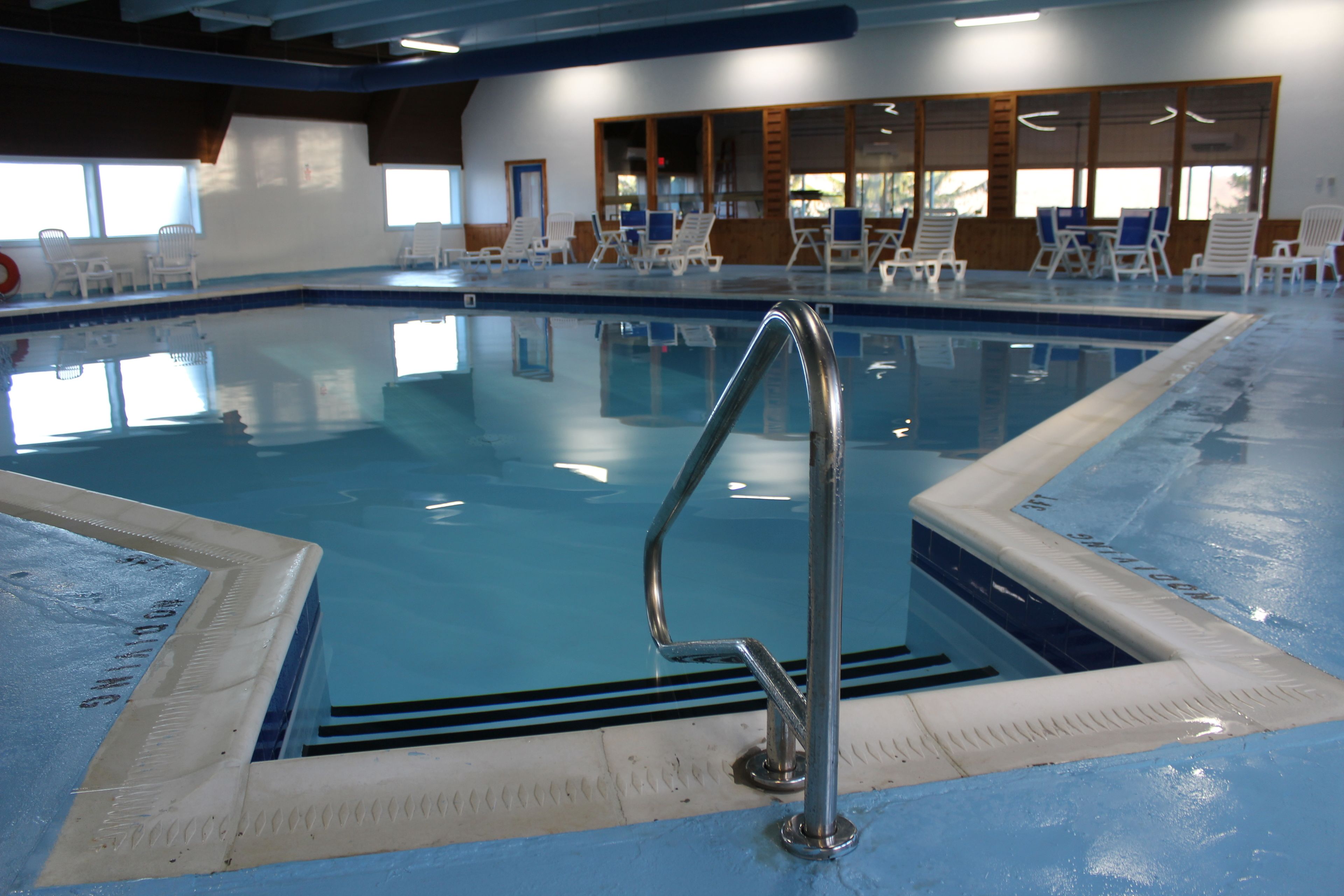 Una piscina interior con una escalera de metal, sillones de descanso y vistas al exterior a través de amplios ventanales.