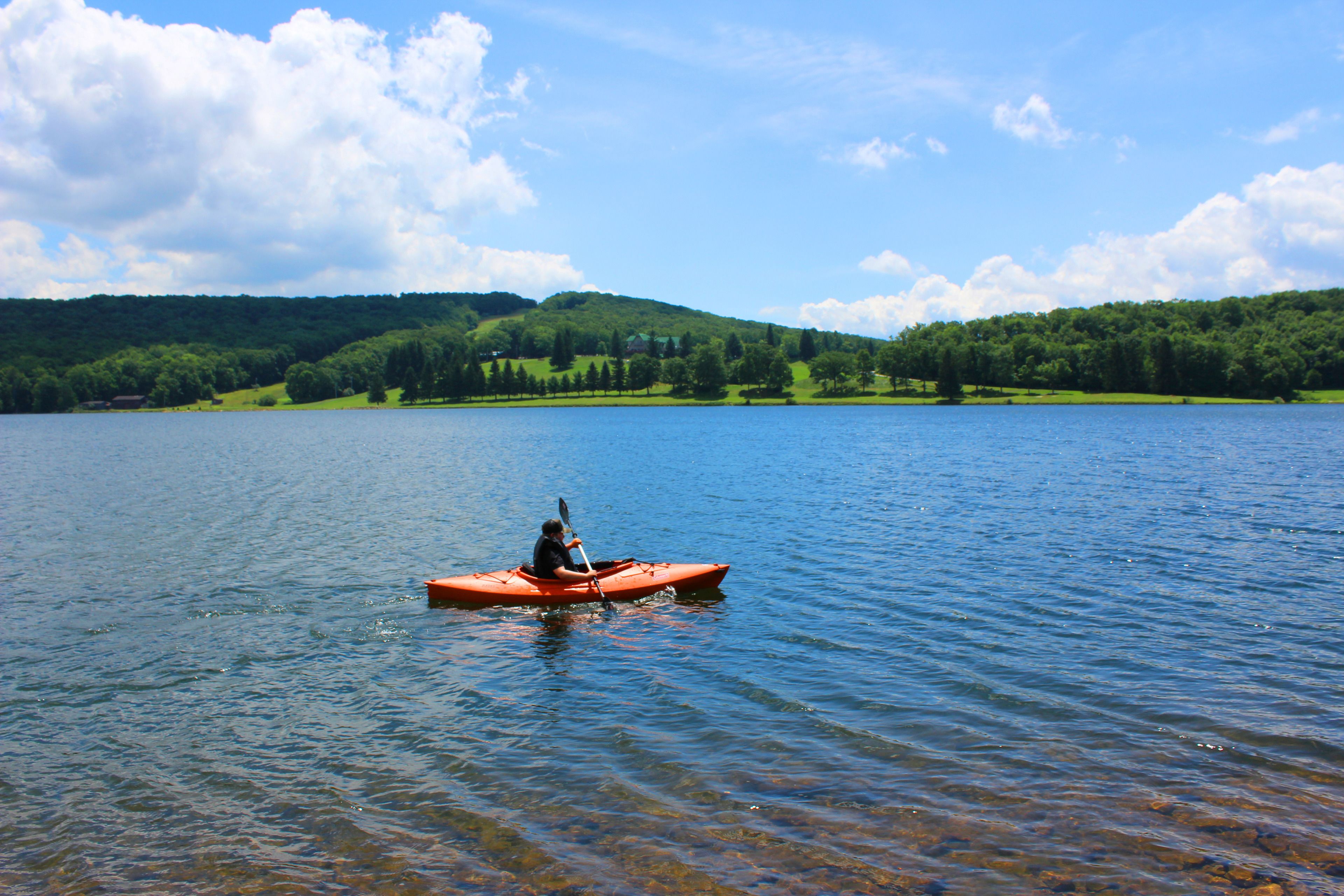 A kayaker on a calm lake surrounded by green hills.