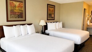 Una camera d'albergo con due letti, un comodino, una lampada e due quadri appesi al muro.