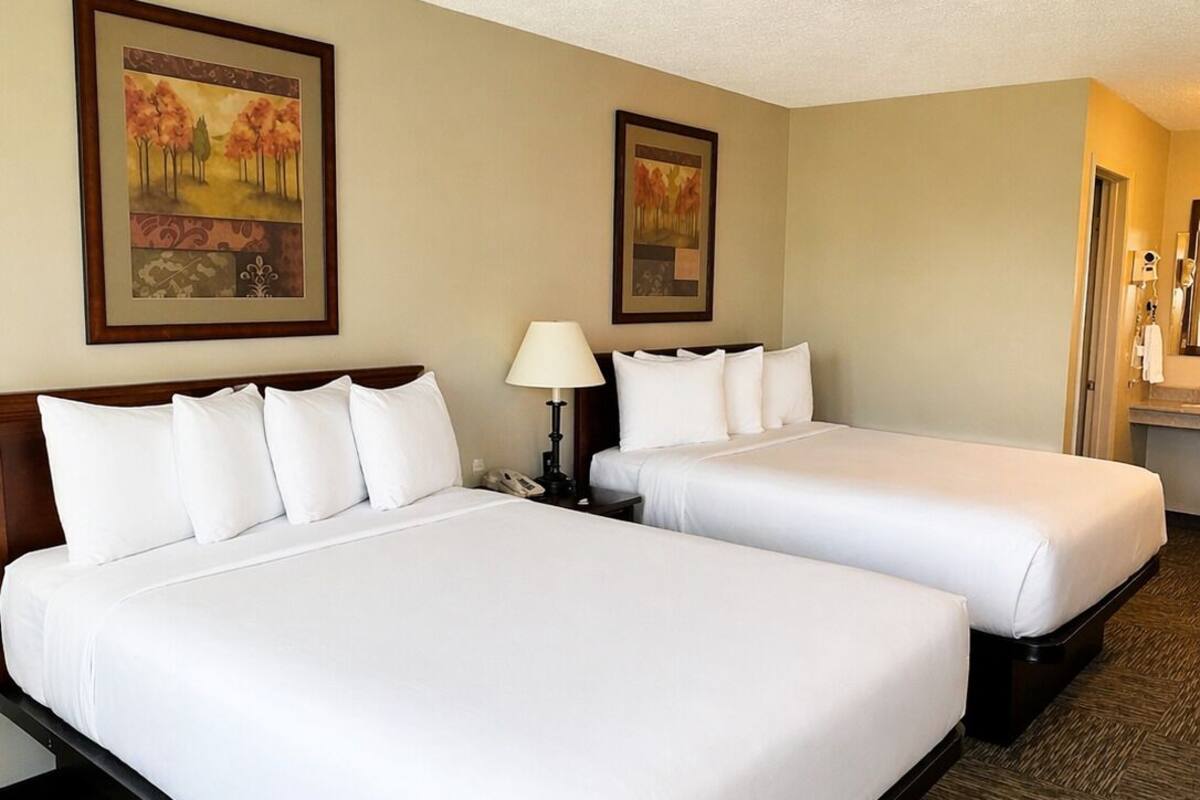 A hotel room with two beds, a nightstand, a lamp, and two framed pictures on the wall.