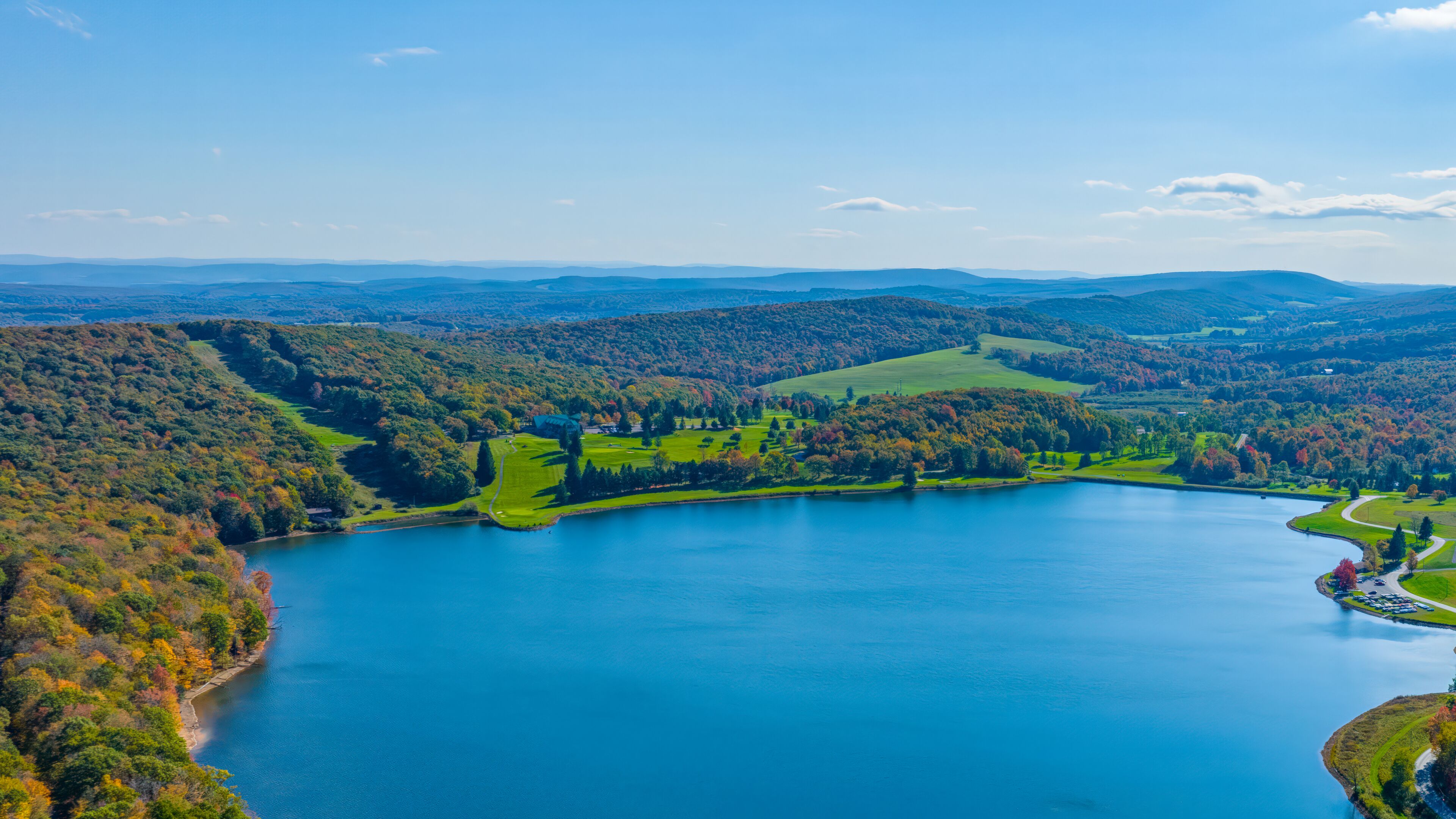 Un lago extenso rodeado de colinas boscosas y un campo de golf.