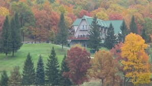 Un grande edificio a più piani con tetto verde, immerso in un paesaggio collinare e rigoglioso con alberi dai colori autunnali.