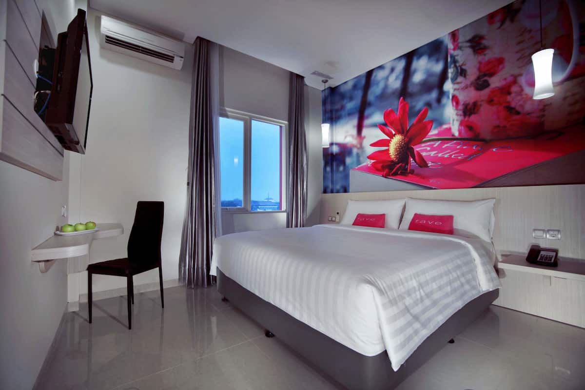 Habitación de hotel moderna con una cama grande, un escritorio con una silla, una mesita con manzanas y una ventana con cortinas.